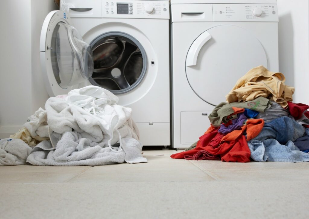 Image of a washing machine and drier with piles of washing in front of them.